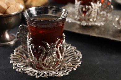Photo of Glass of traditional Turkish tea in vintage holder on black table, closeup. Space for text