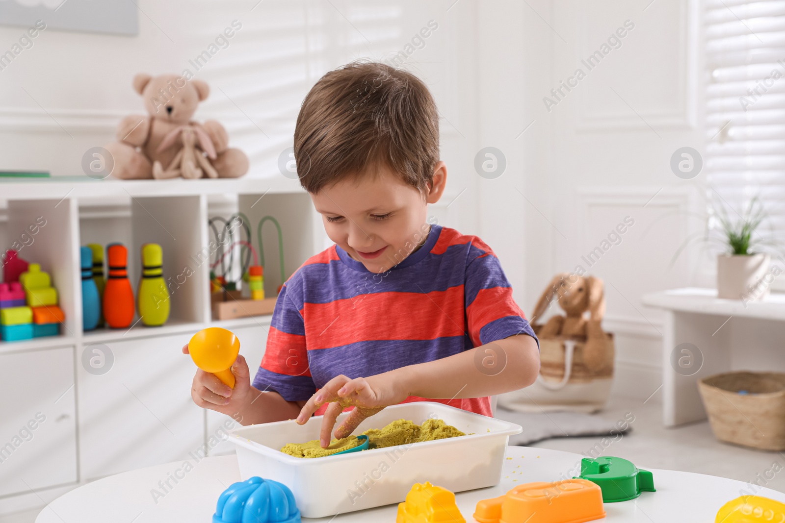 Photo of Cute little boy playing with bright kinetic sand at table in room