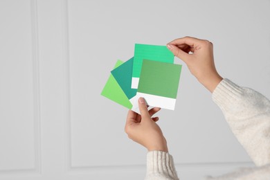 Photo of Woman with color sample cards choosing paint shade for wall indoors, closeup. Interior design