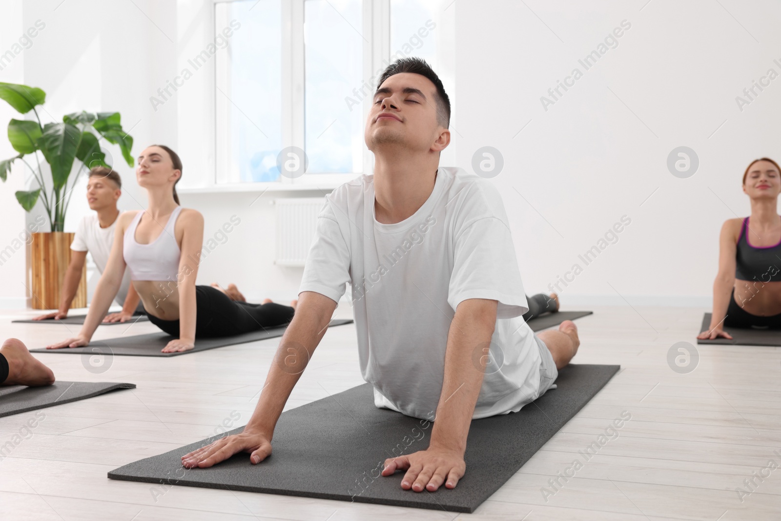 Photo of Young man practicing yoga during group lesson indoors