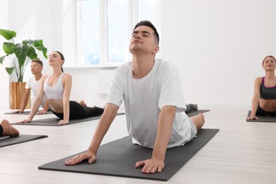 Photo of Young man practicing yoga during group lesson indoors