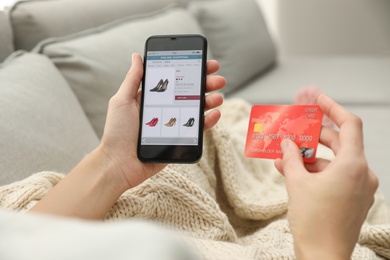 Woman with credit card using smartphone for online shopping indoors, closeup