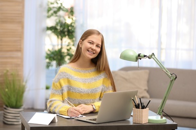 Photo of Pretty teenage girl doing homework at table in room