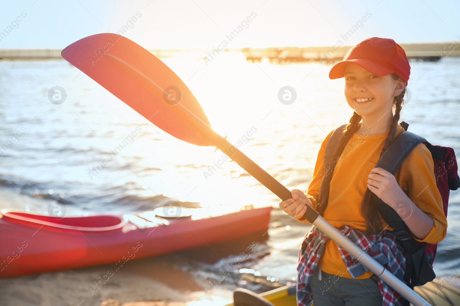 Photo of Happy girl with paddle near kayak on river shore. Summer camp activity