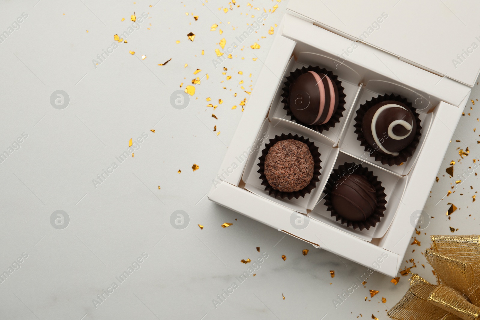 Photo of Different delicious chocolate truffles in box, bow and confetti on white background, flat lay. Space for text