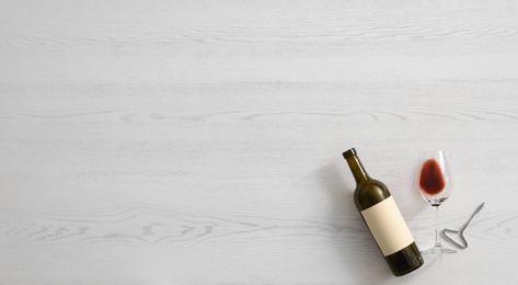 Flat lay composition with bottle of wine and elegant glass on white wooden background. Space for text