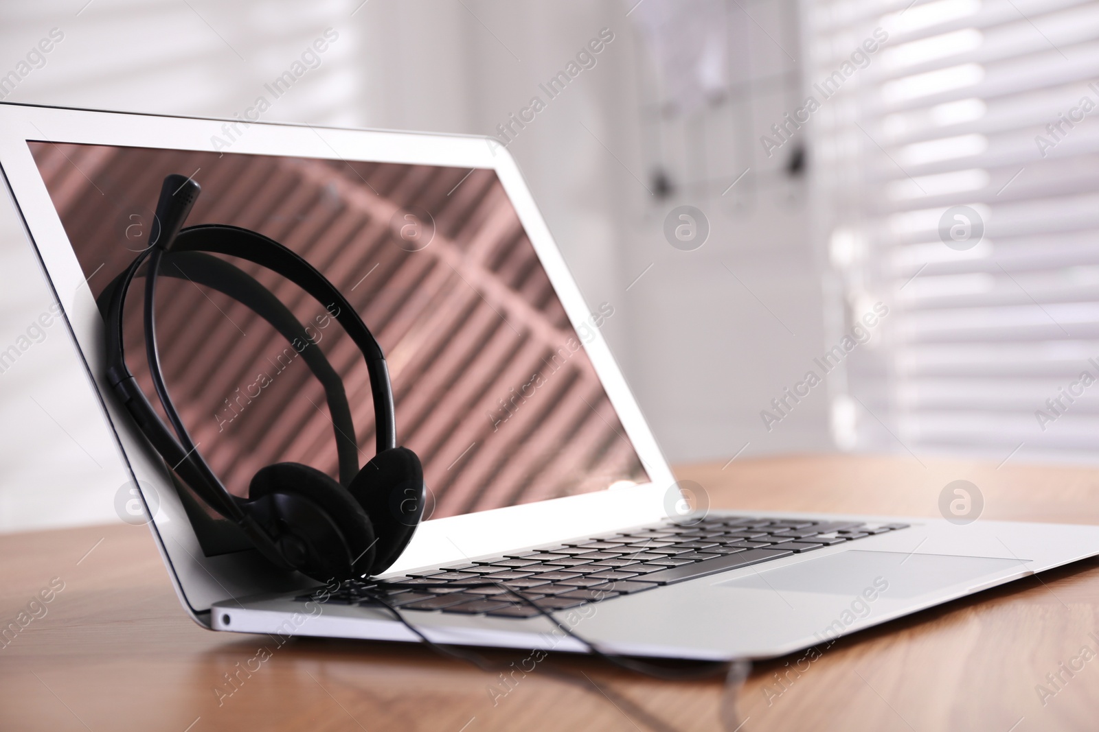 Photo of Modern laptop with headset on wooden table in office, space for text. Hotline service