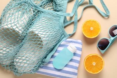 Photo of String bag, different beach accessories and orange on beige background, flat lay