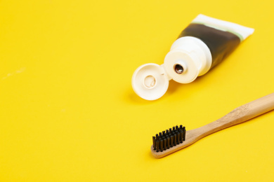 Photo of Toothbrush made of bamboo and charcoal paste on yellow background, space for text