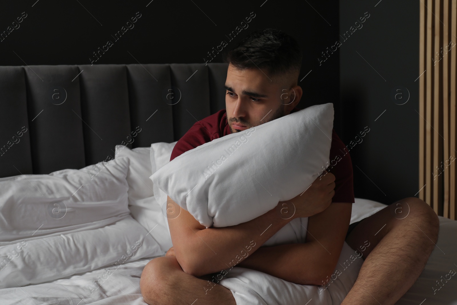 Photo of Sad man hugging pillow on bed at home. Space for text