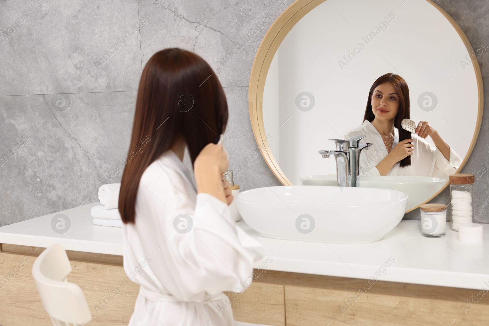 Photo of Beautiful woman brushing her hair near mirror in bathroom