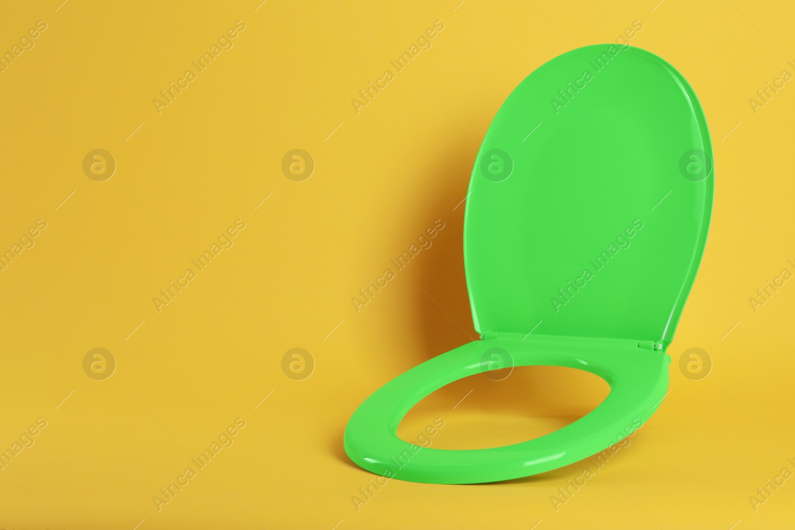 Photo of New green plastic toilet seat on yellow background, space for text