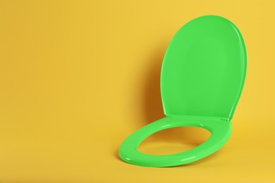 New green plastic toilet seat on yellow background, space for text