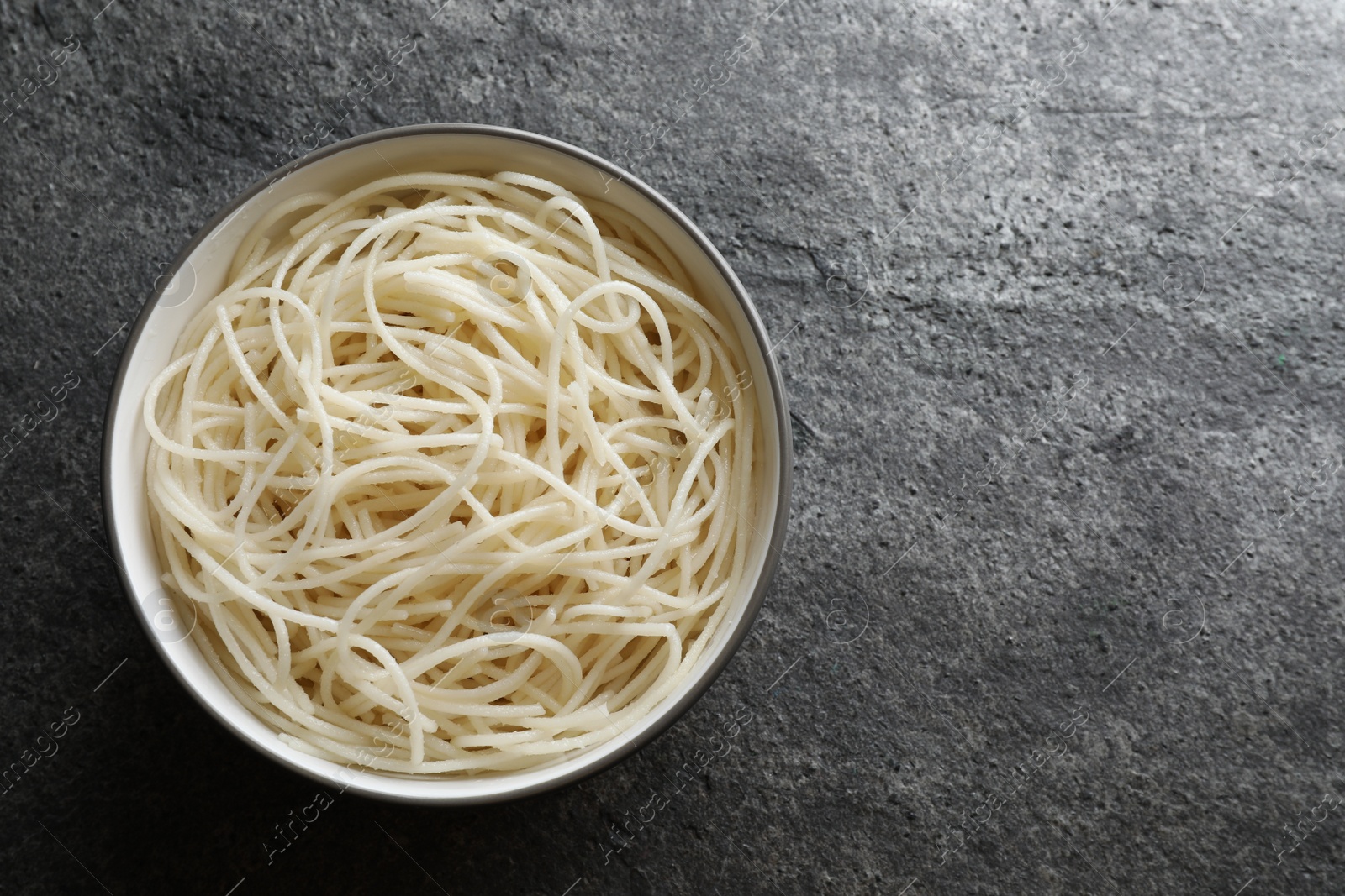 Photo of Bowl of tasty cooked rice noodles on grey table, top view. Space for text