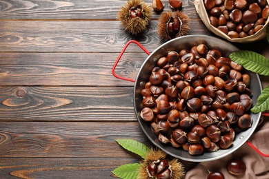 Delicious roasted edible chestnuts on brown wooden table, flat lay. Space for text