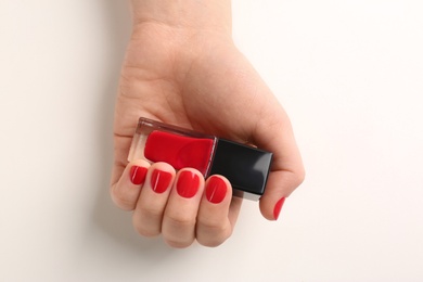 Photo of Woman with red manicure holding nail polish bottle on white background, top view