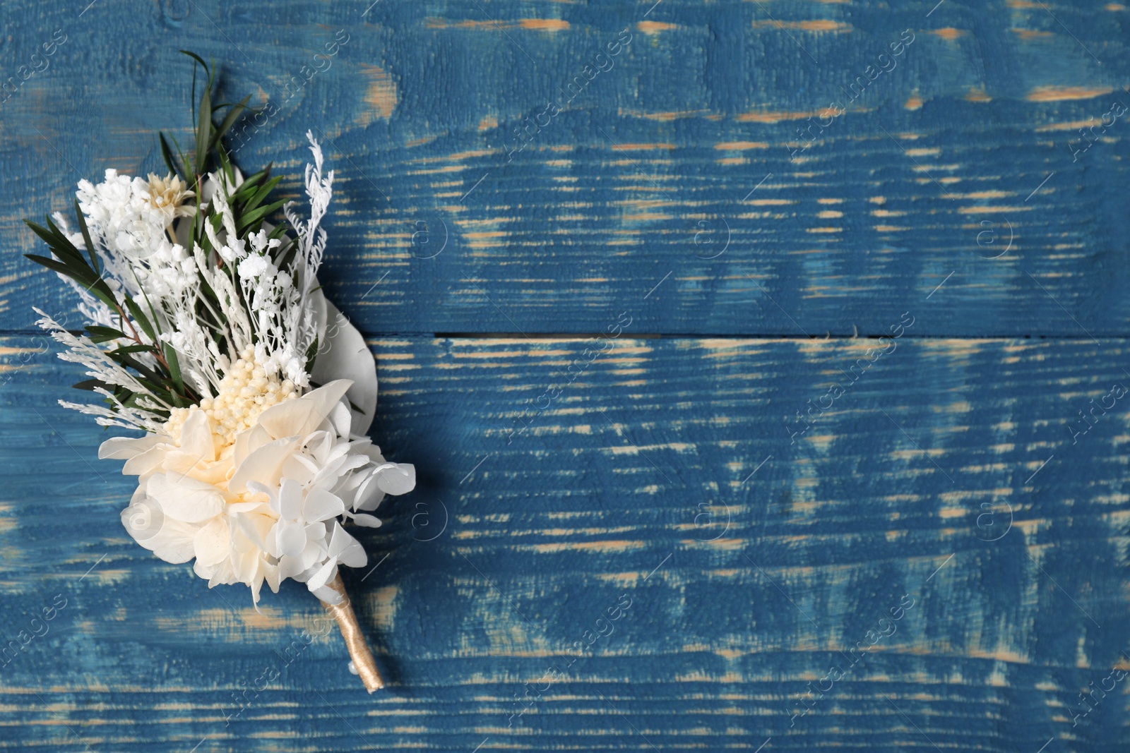 Photo of Stylish white boutonniere on blue wooden table, top view. Space for text