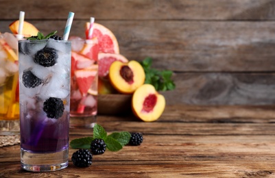 Photo of Delicious blackberry lemonade made with soda water and fresh ingredients on wooden table. Space for text