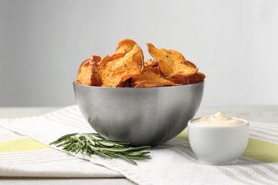 Photo of Bowl of sweet potato chips with sauce and rosemary on table against light background