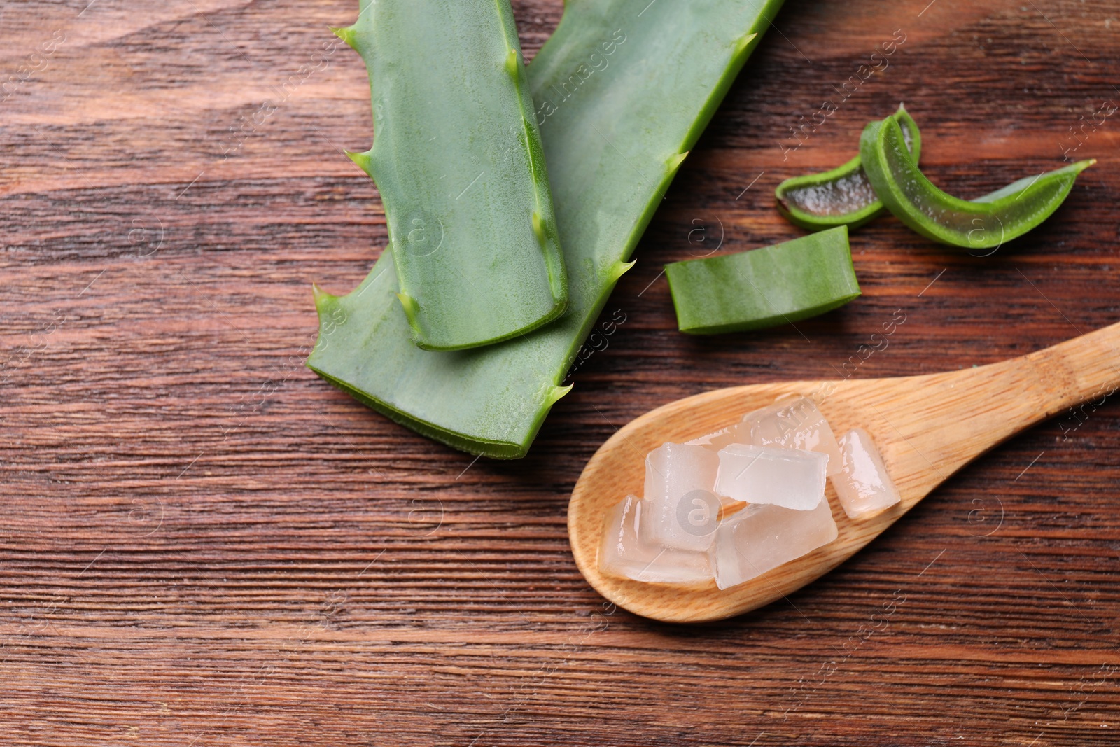 Photo of Aloe vera gel and slices of plant on wooden table, flat lay. Space for text