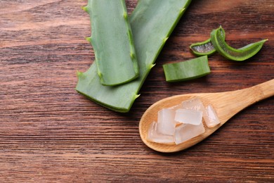 Aloe vera gel and slices of plant on wooden table, flat lay. Space for text