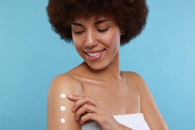 Photo of Beautiful young woman applying body cream onto arm on light blue background
