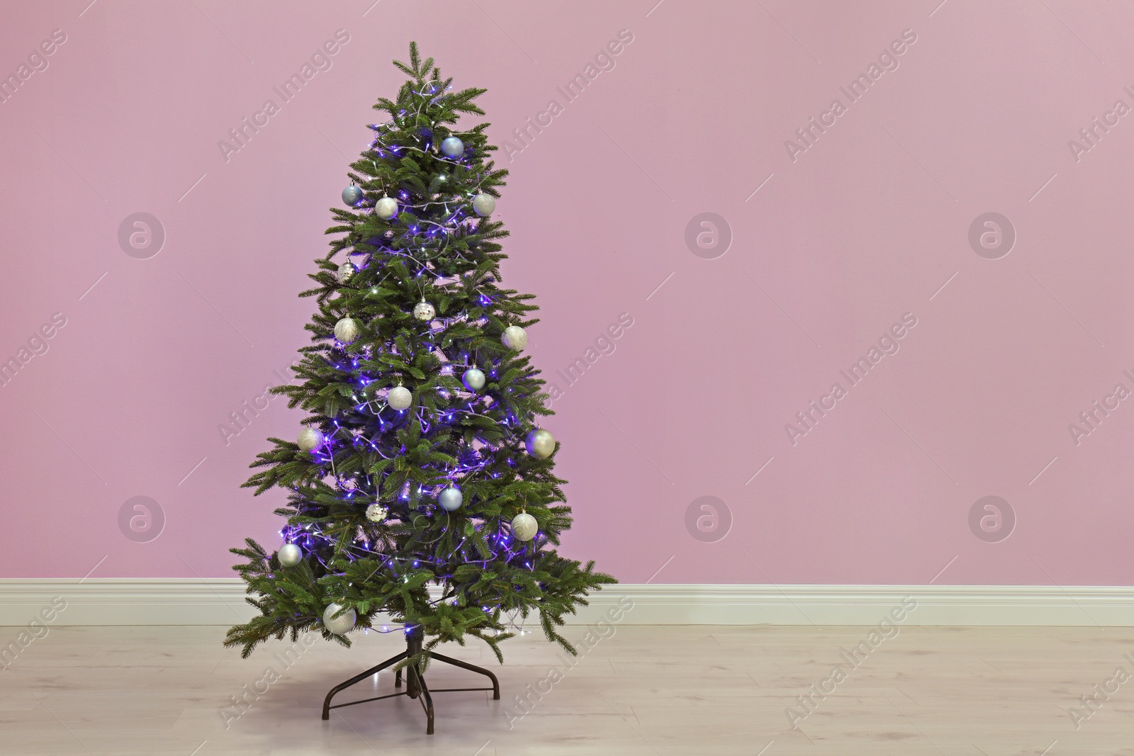 Photo of Beautiful Christmas tree with decor near color wall indoors. Celebration time