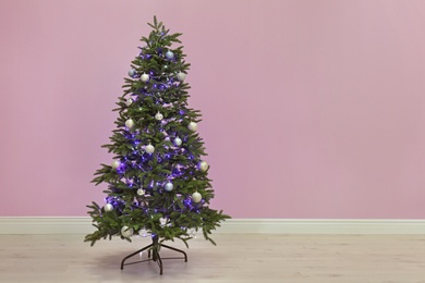 Photo of Beautiful Christmas tree with decor near color wall indoors. Celebration time