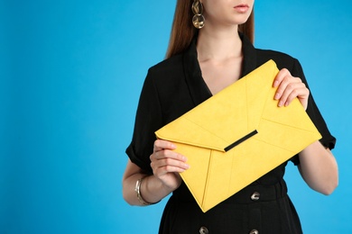 Young woman with stylish yellow bag on light blue background, closeup. Space for text