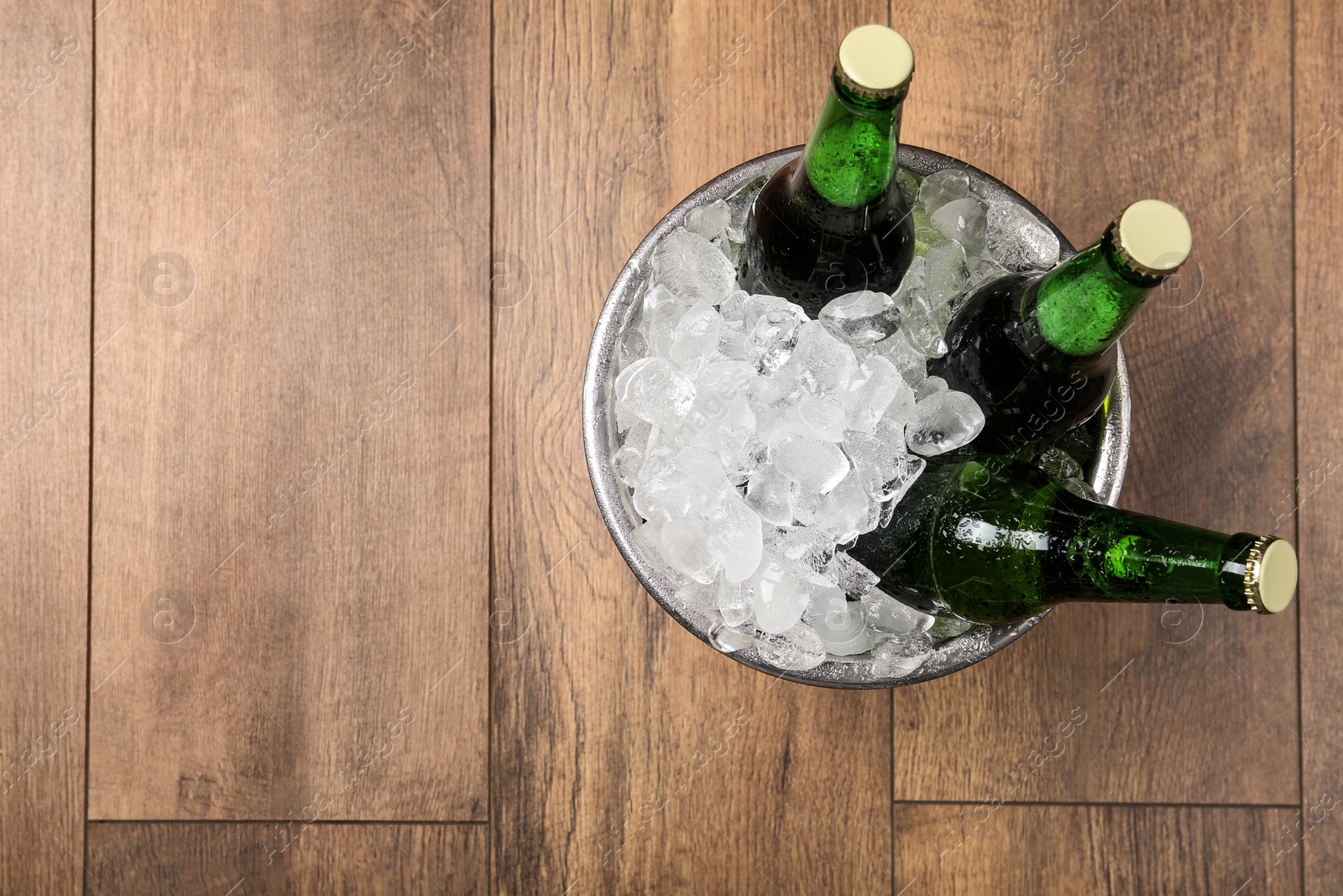Photo of Beer in metal bucket with ice on wooden background, top view. Space for text