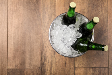 Photo of Beer in metal bucket with ice on wooden background, top view. Space for text