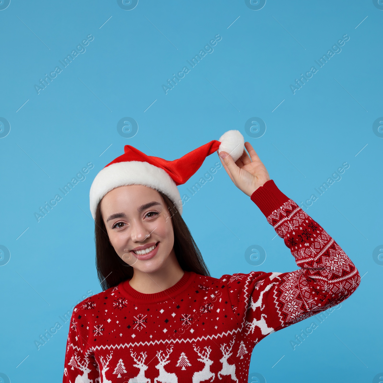 Photo of Happy young woman in Christmas sweater and Santa hat on light blue background