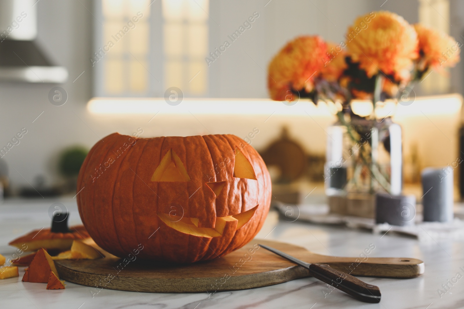 Photo of Pumpkin jack o'lantern on white marble table in kitchen, space for text. Halloween celebration