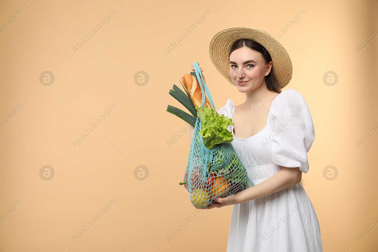 Photo of Woman with string bag of fresh vegetables and baguette on beige background, space for text