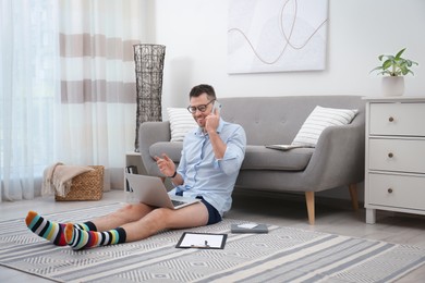 Businessman in shirt and underwear talking on phone during video call at home