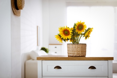 Beautiful yellow sunflowers on chest of drawers in room, space for text