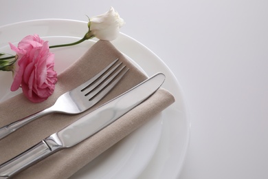 Photo of Elegant cutlery with napkin and flowers on white table, closeup