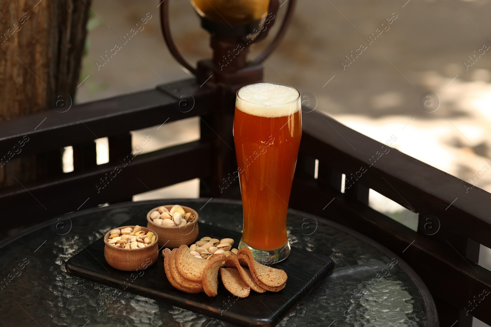 Photo of Glass of tasty beer served with snacks on table outdoors