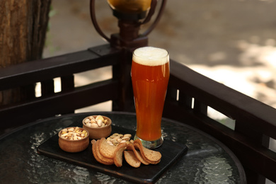 Glass of tasty beer served with snacks on table outdoors