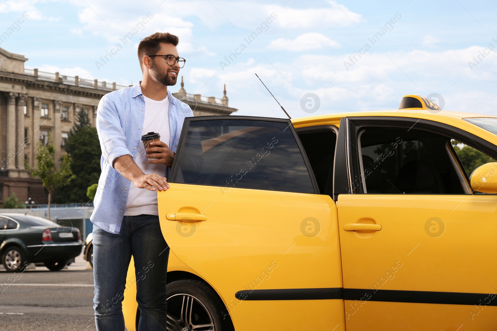 Photo of Handsome young man with coffee getting out of taxi on city street