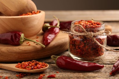 Photo of Chili pepper flakes and pods on wooden table, closeup