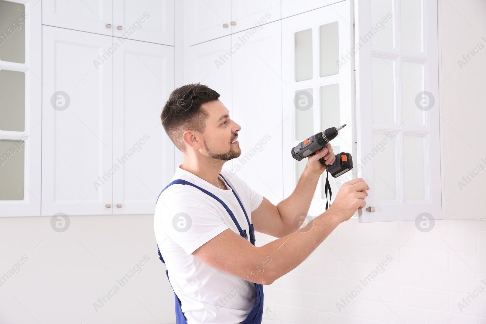 Photo of Worker installing handle on cabinet door with screw gun in kitchen