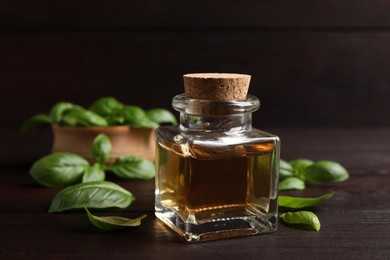 Bottle of basil essential oil and green leaves on wooden table