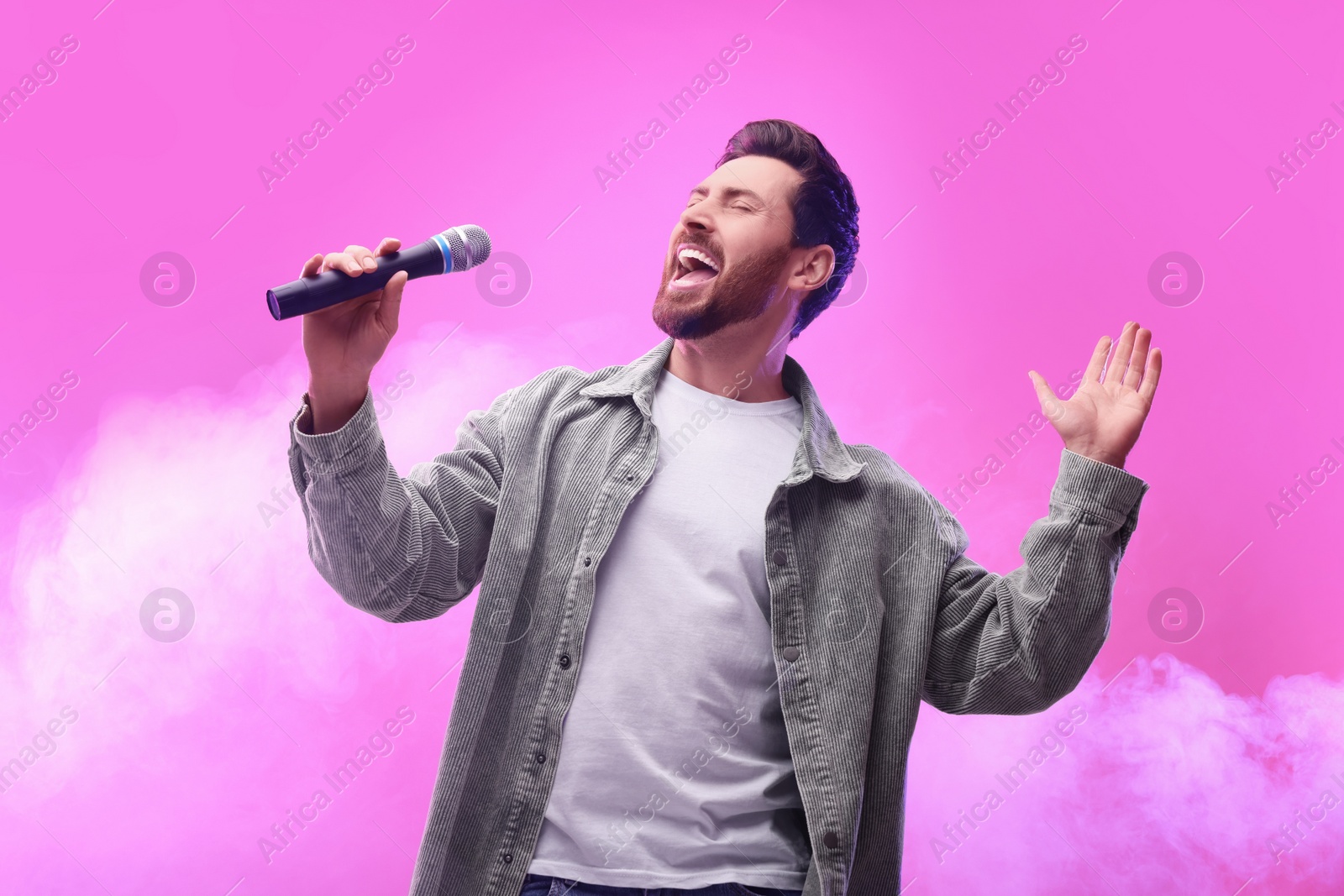 Photo of Handsome man with microphone singing on pink background