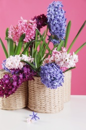 Photo of Beautiful hyacinths in wicker pots on table against color background. Spring flowers