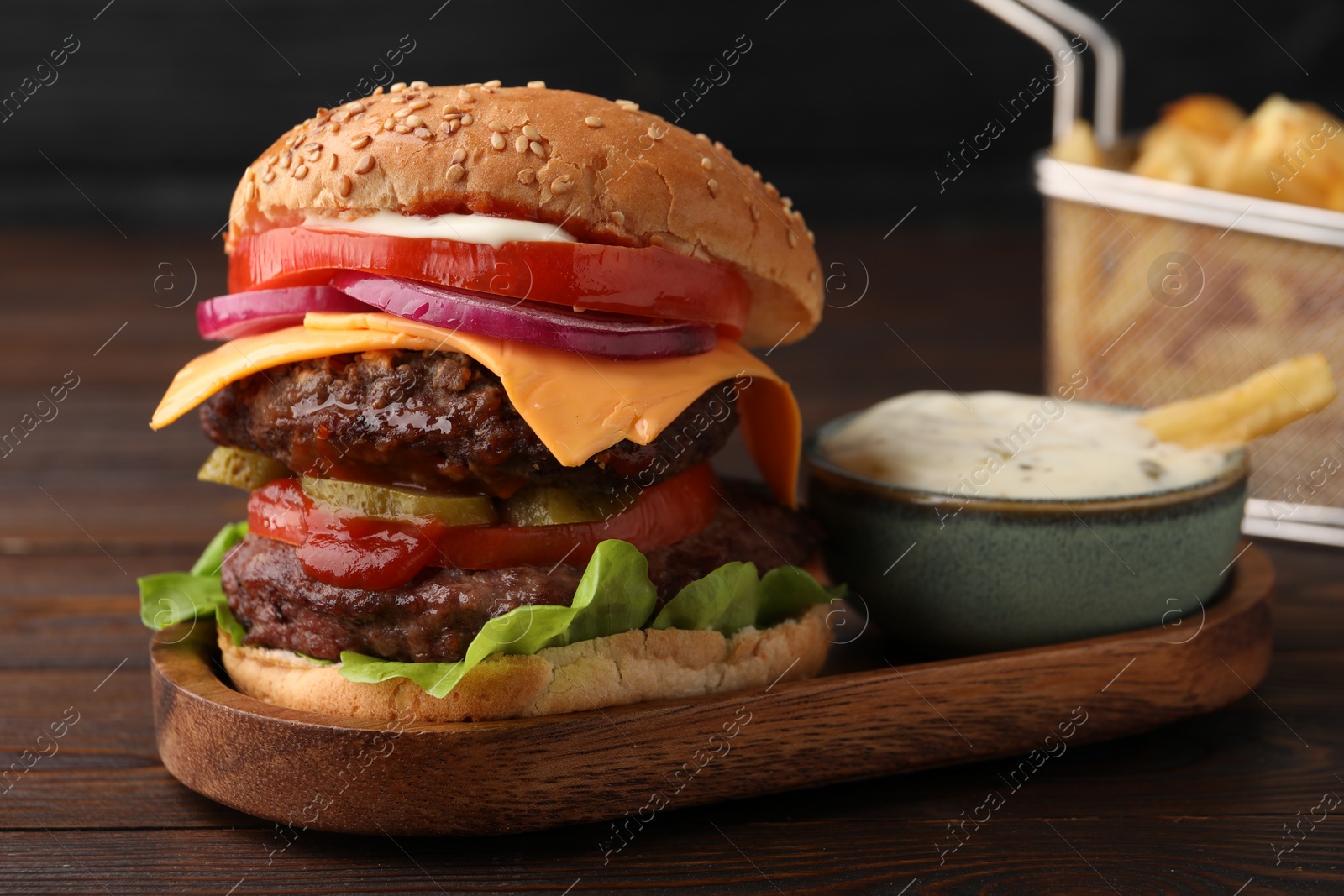 Photo of Tasty cheeseburger with patties, tomato and sauce on wooden table, closeup