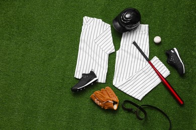 Photo of Baseball uniform and other sports equipment on artificial grass, flat lay. Space for text