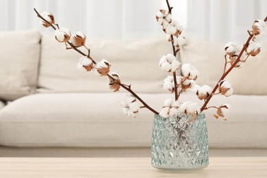 Cotton branches with fluffy flowers on wooden table in cozy room. Space for text