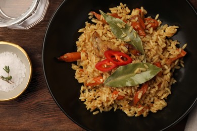 Photo of Delicious pilaf, bay leaves, glass of water and salt on wooden table, flat lay