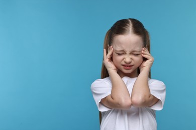 Photo of Little girl suffering from headache on light blue background. Space for text